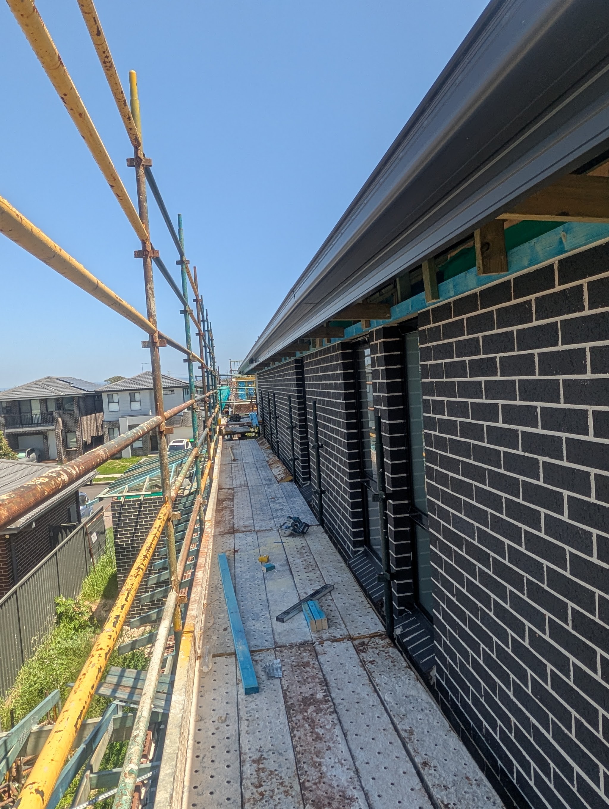 View along a scaffold beside a dark brick two-storey new build, fascia and gutter fitted