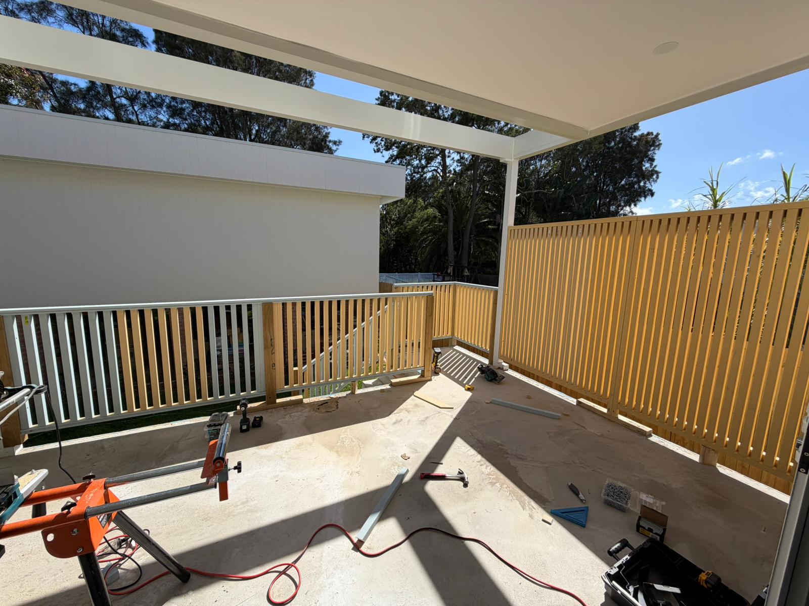 Painted timber slat privacy screen and balustrade on a covered deck, tools laid out on the slab