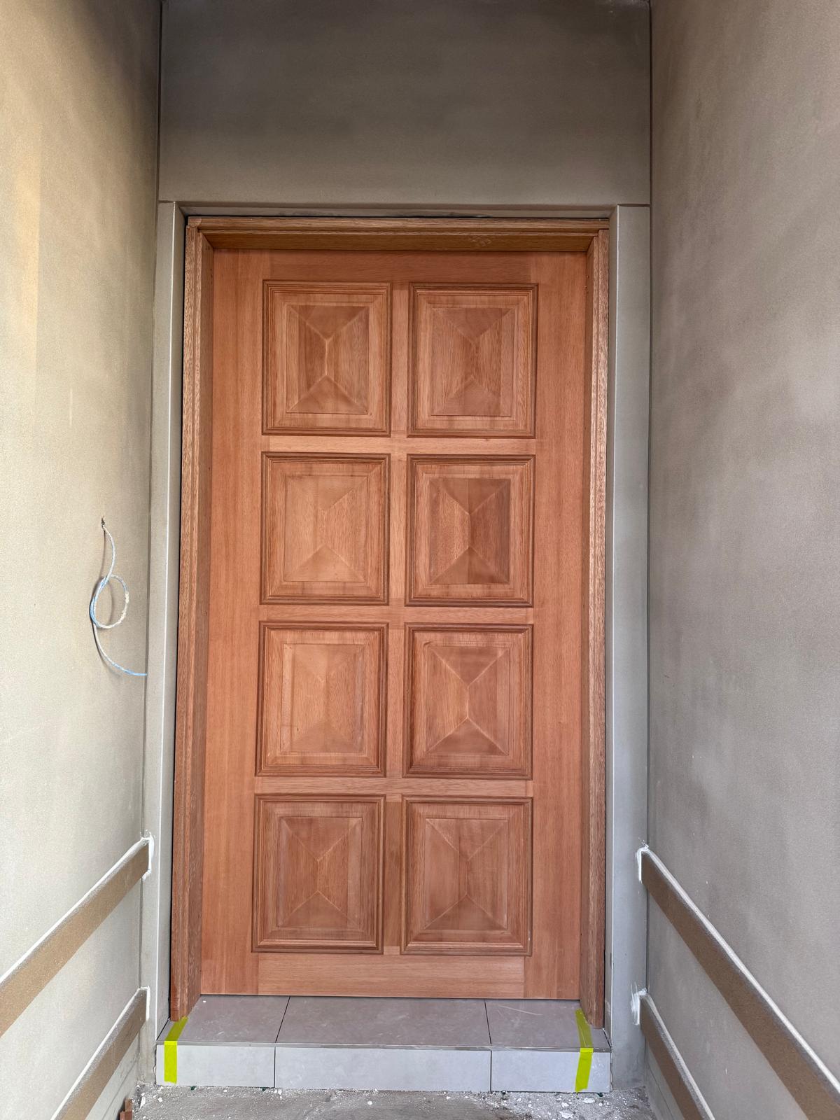 Stained eight-panel timber entry door set into a rendered porch